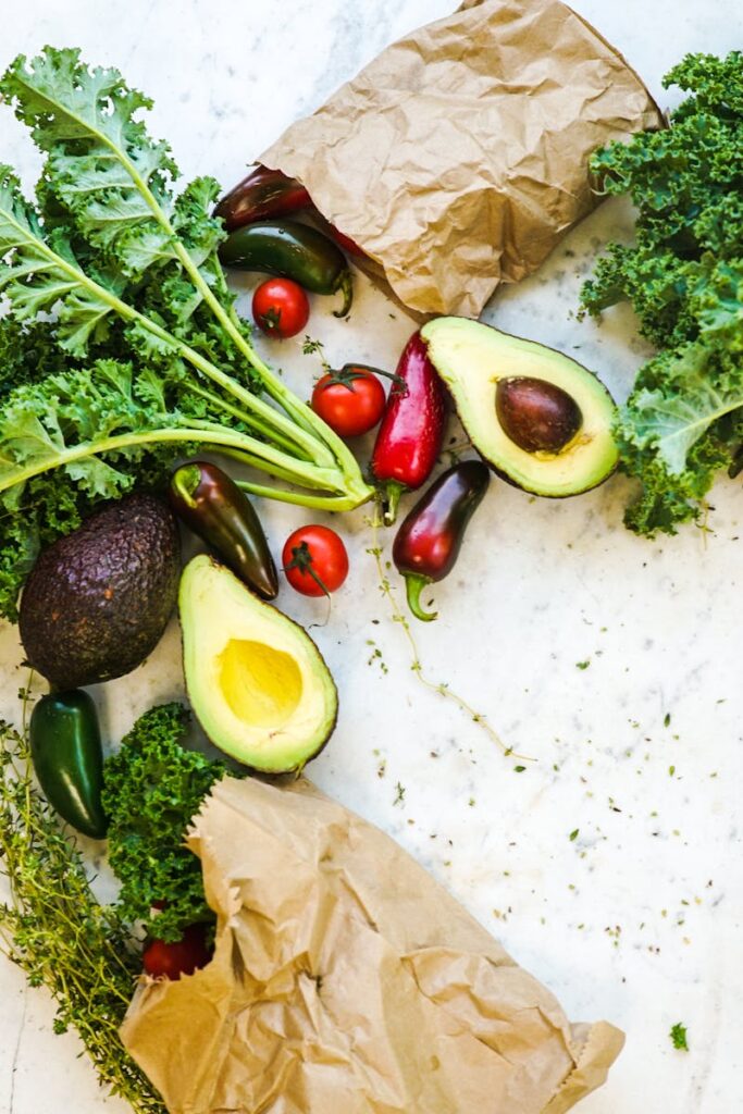 Avocado, kale, and more fresh produce artfully arranged on a marble surface.
